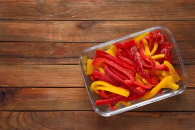 Photo of Slices of frozen bell peppers in glass container on wooden table, top view. Space for text