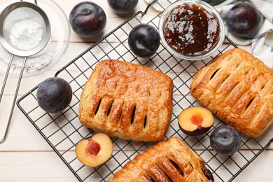 Photo of Delicious puff pastries and plums on white wooden table, flat lay