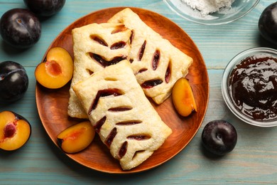 Delicious puff pastries, plums and jam on light blue wooden table, top view