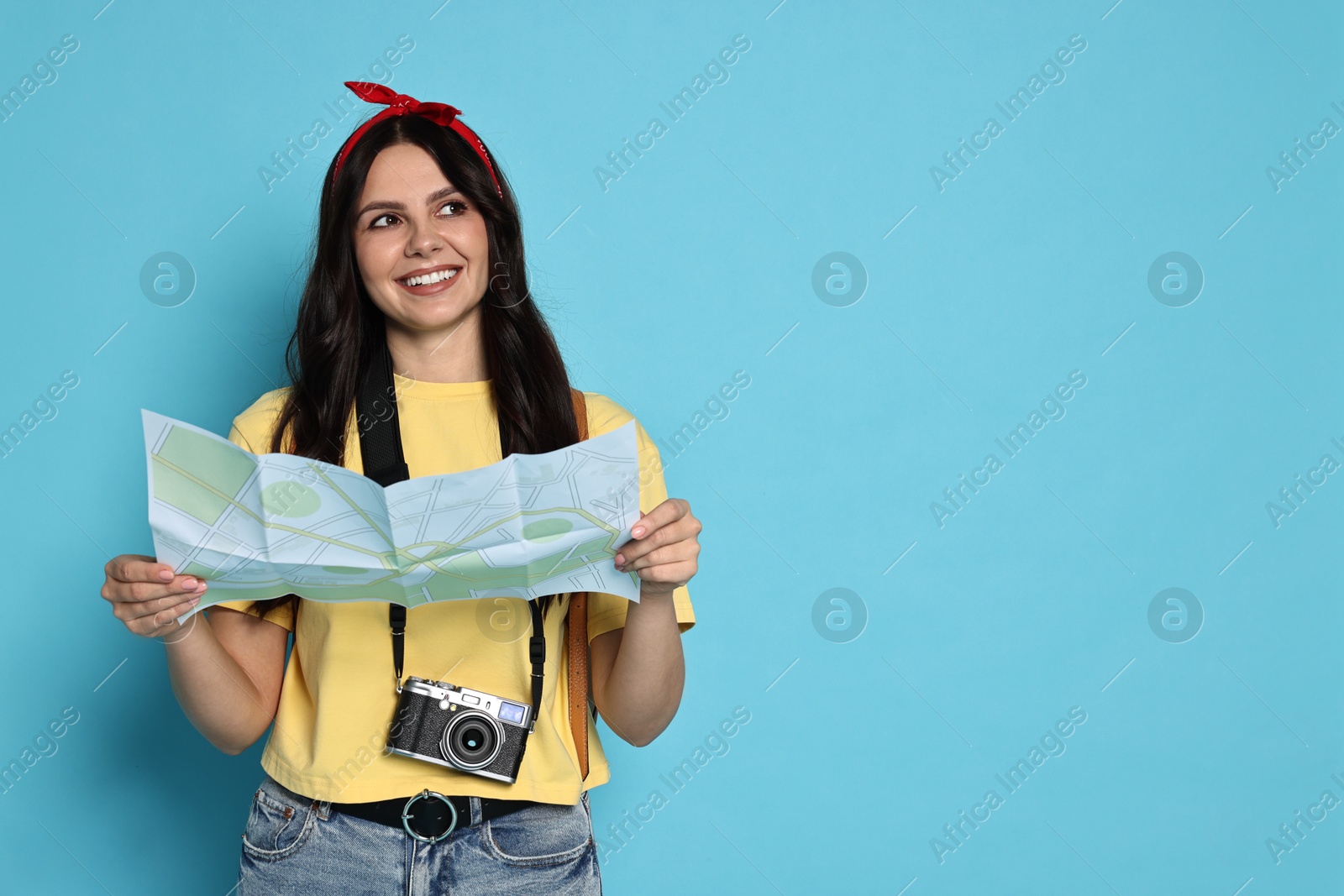 Photo of Young tourist in hat with camera and map on light blue background, space for text