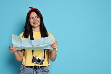 Photo of Young tourist in hat with camera and map on light blue background, space for text