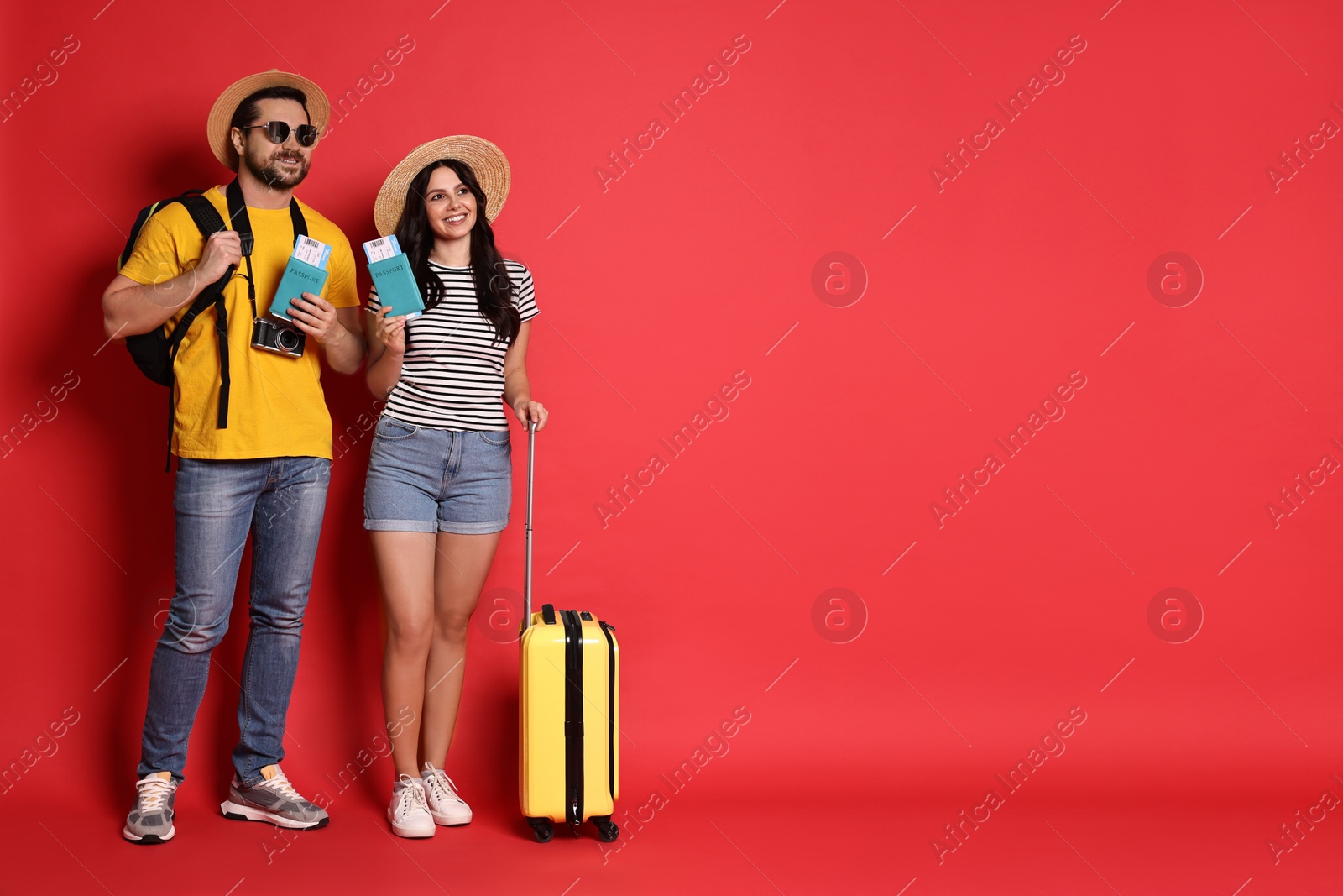 Photo of Tourism. Happy couple in hats with suitcase, passports and tickets on red background, space for text