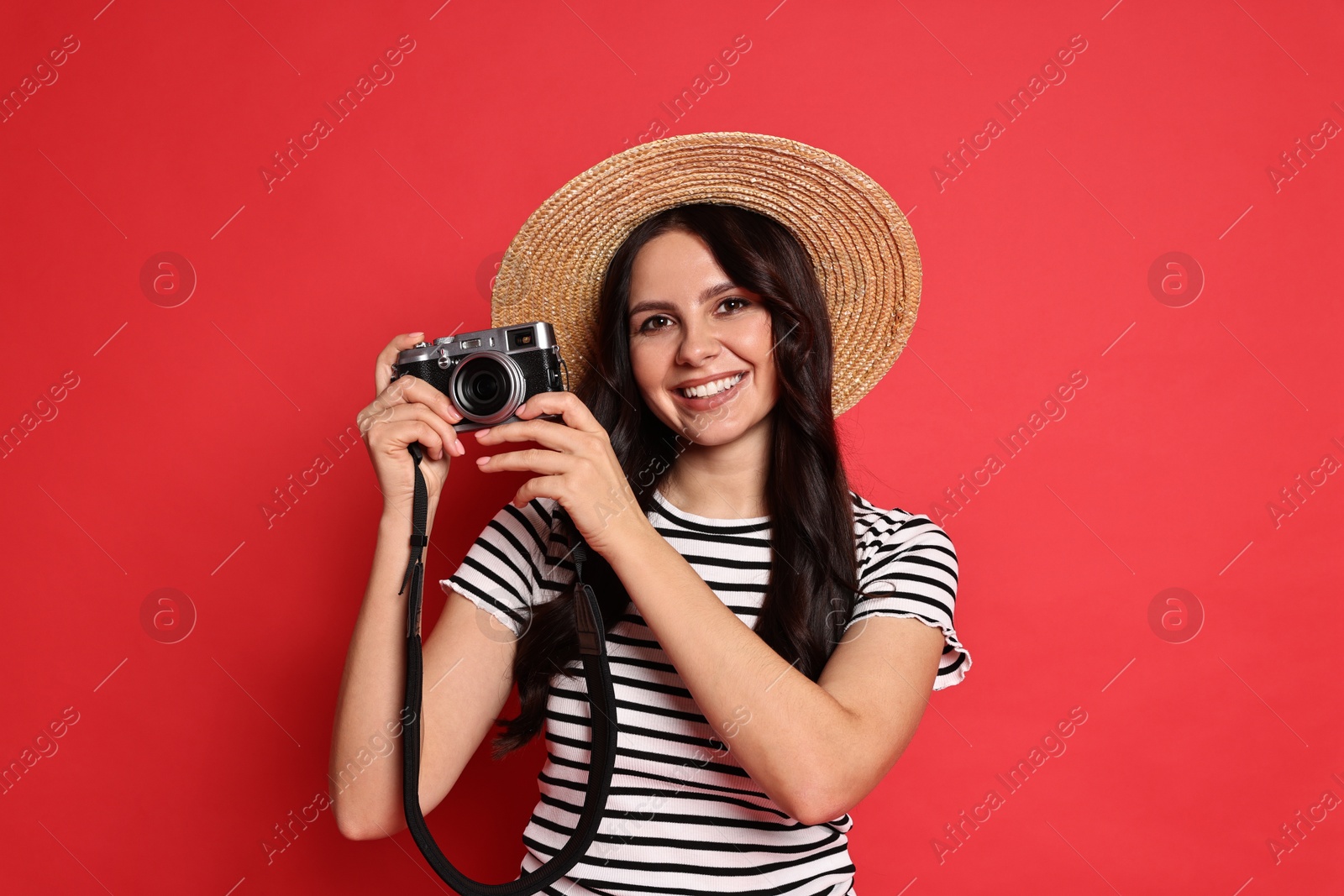 Photo of Young tourist in hat with camera on red background