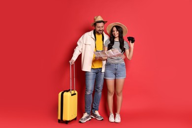 Photo of Tourism. Happy couple in hats with suitcase, map and binoculars on red background