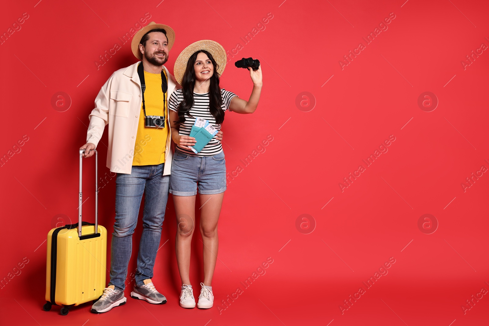 Photo of Tourism. Happy couple in hats with suitcase, binoculars passports and tickets on red background