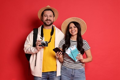 Photo of Tourism. Happy couple in hats with camera, passports and tickets on red background