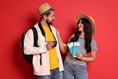 Tourism. Happy couple in hats with camera, passports and tickets on red background