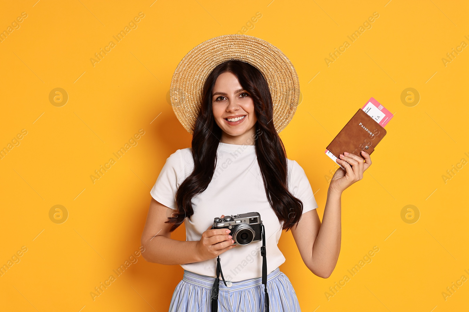 Photo of Young tourist in hat with camera, passport and ticket on yellow background