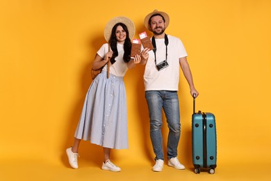 Photo of Tourism. Happy couple in hats with suitcase, passports and tickets on yellow background