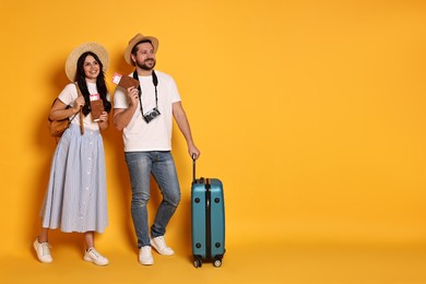 Tourism. Happy couple in hats with suitcase, passports and tickets on yellow background, space for text