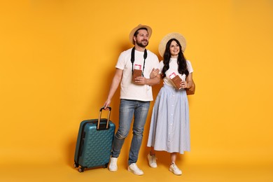 Tourism. Happy couple in hats with suitcase, passports and tickets on yellow background