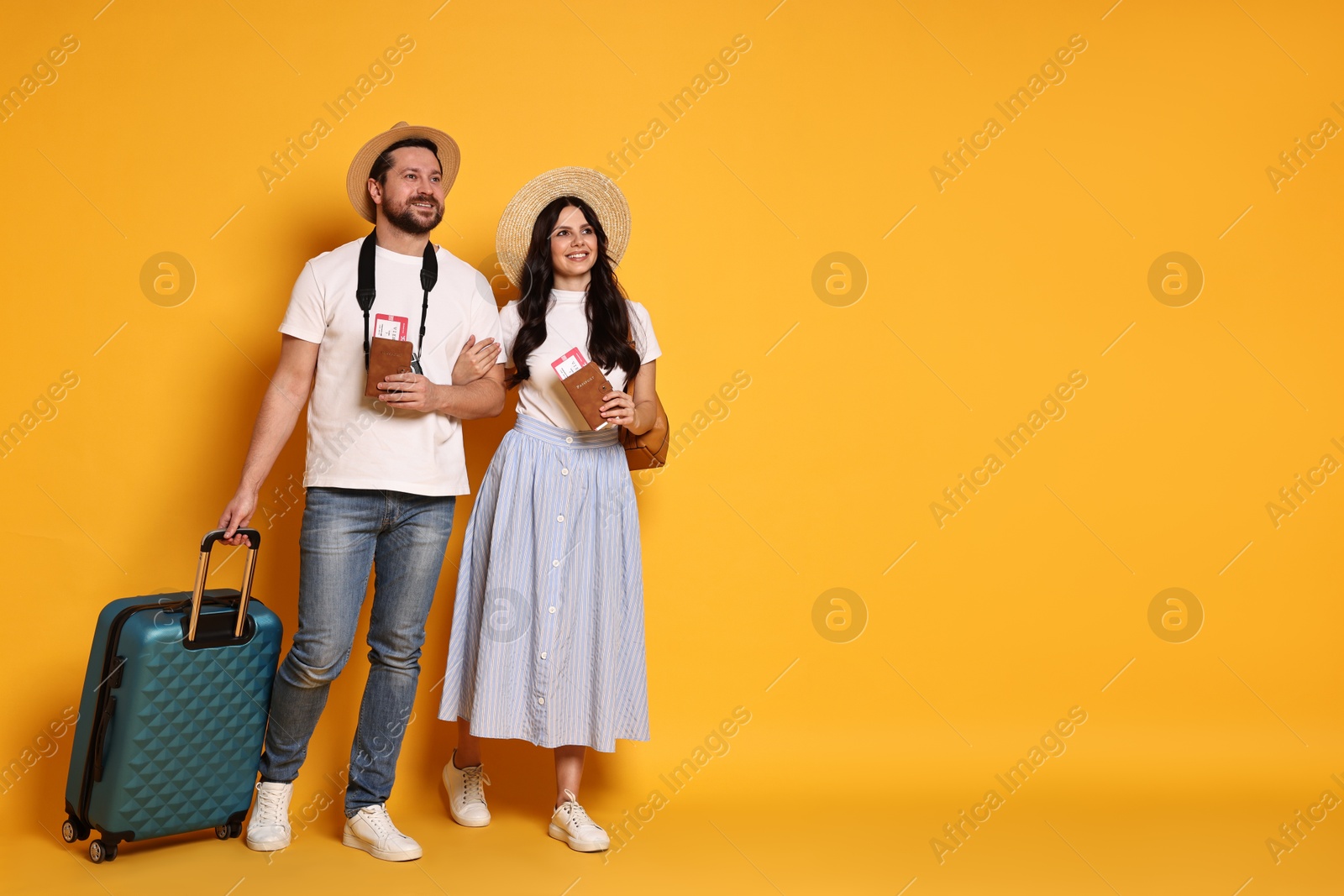 Photo of Tourism. Happy couple in hats with suitcase, passports and tickets on yellow background, space for text