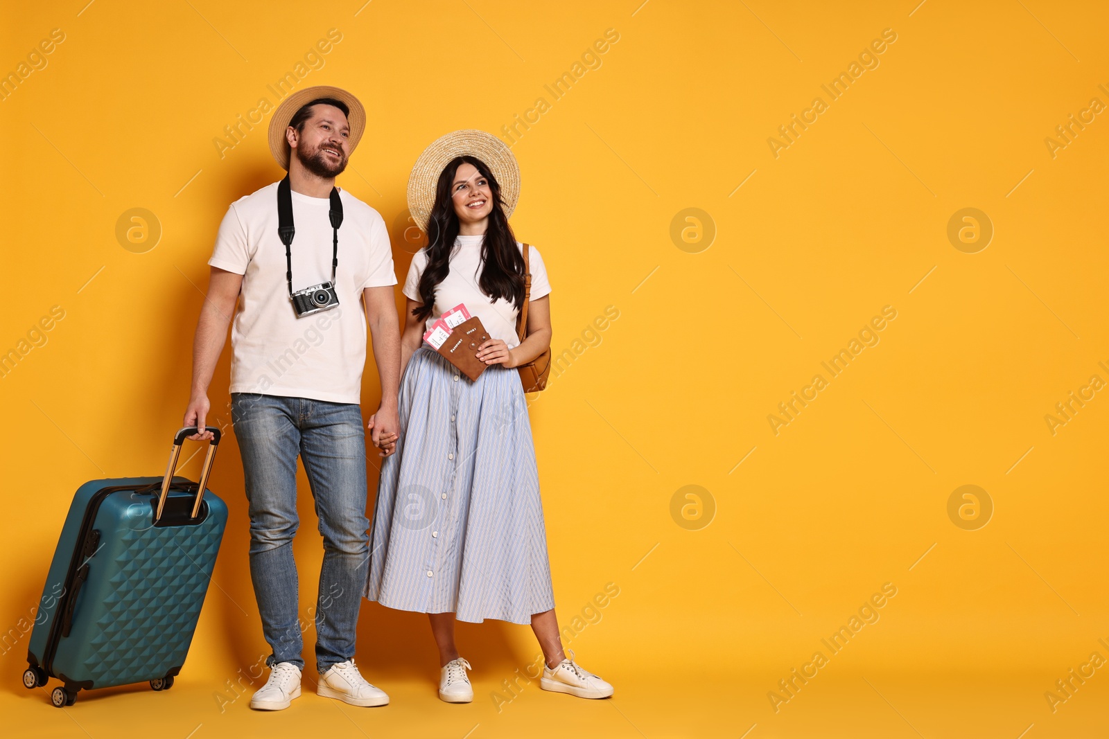 Photo of Tourism. Happy couple in hats with suitcase, passports and tickets on yellow background, space for text