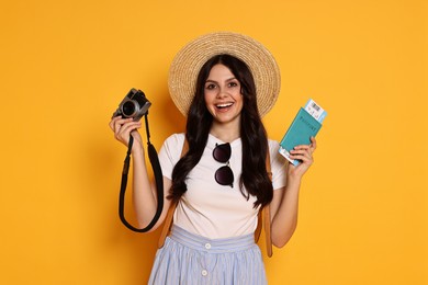 Young tourist in hat with camera, passport and ticket on yellow background