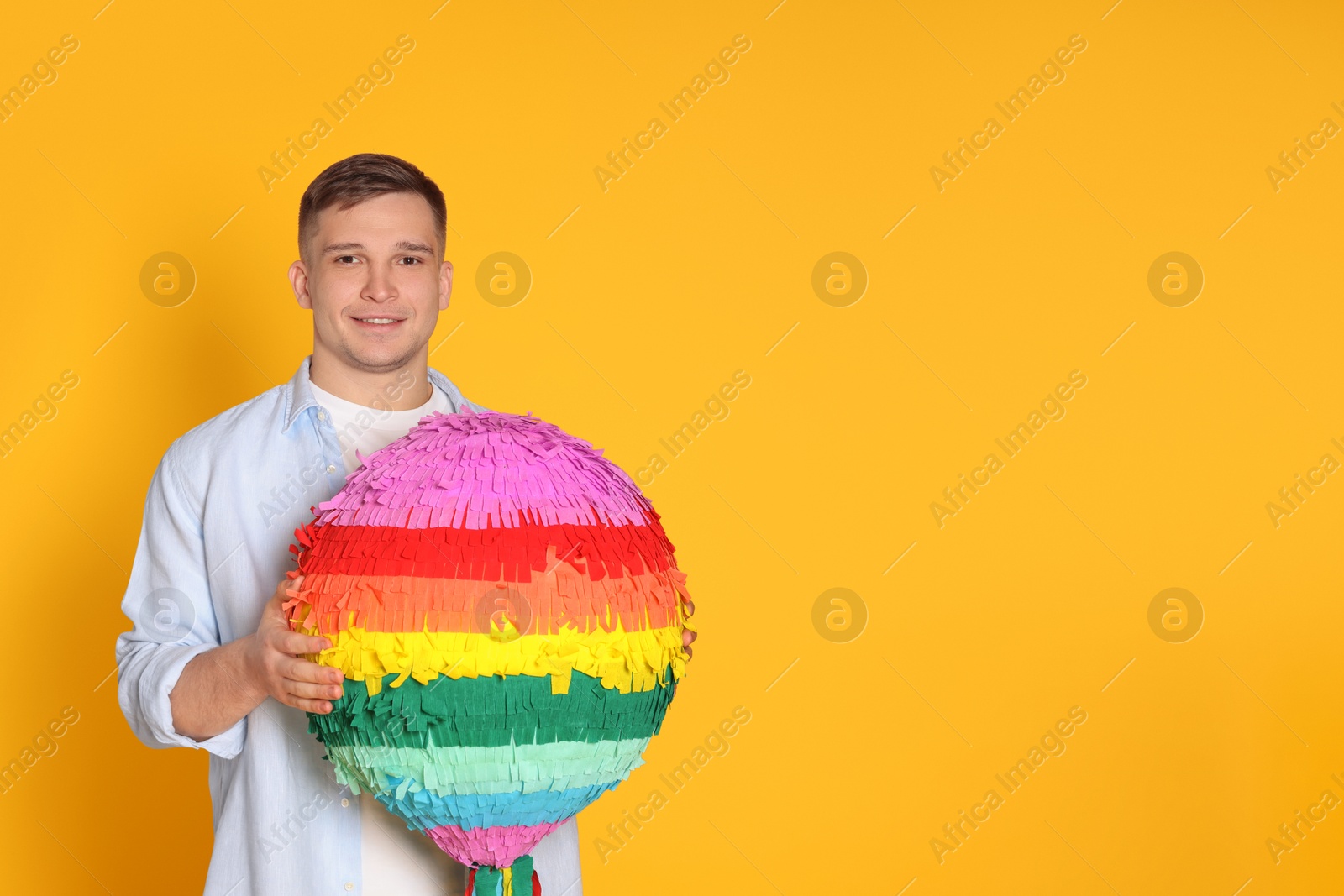 Photo of Happy man with colorful pinata on yellow background. Space for text