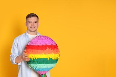 Photo of Happy man with colorful pinata on yellow background. Space for text