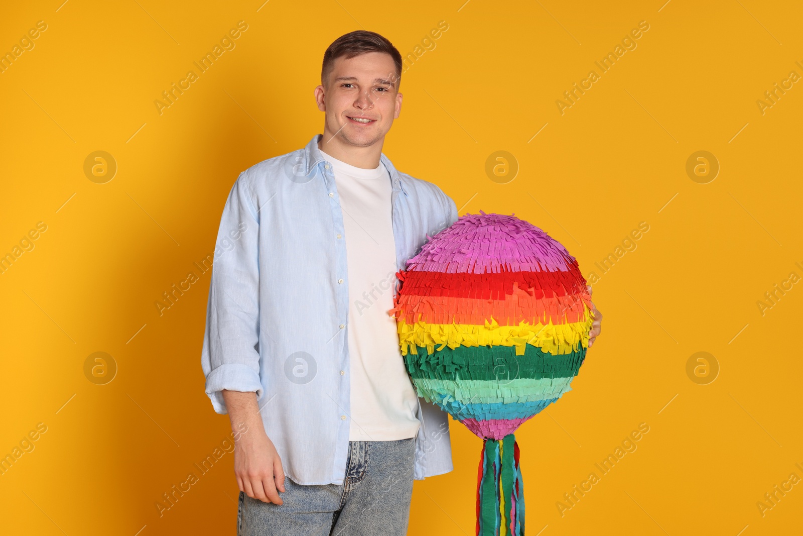 Photo of Happy man with colorful pinata on yellow background