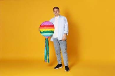 Photo of Happy man with colorful pinata on yellow background