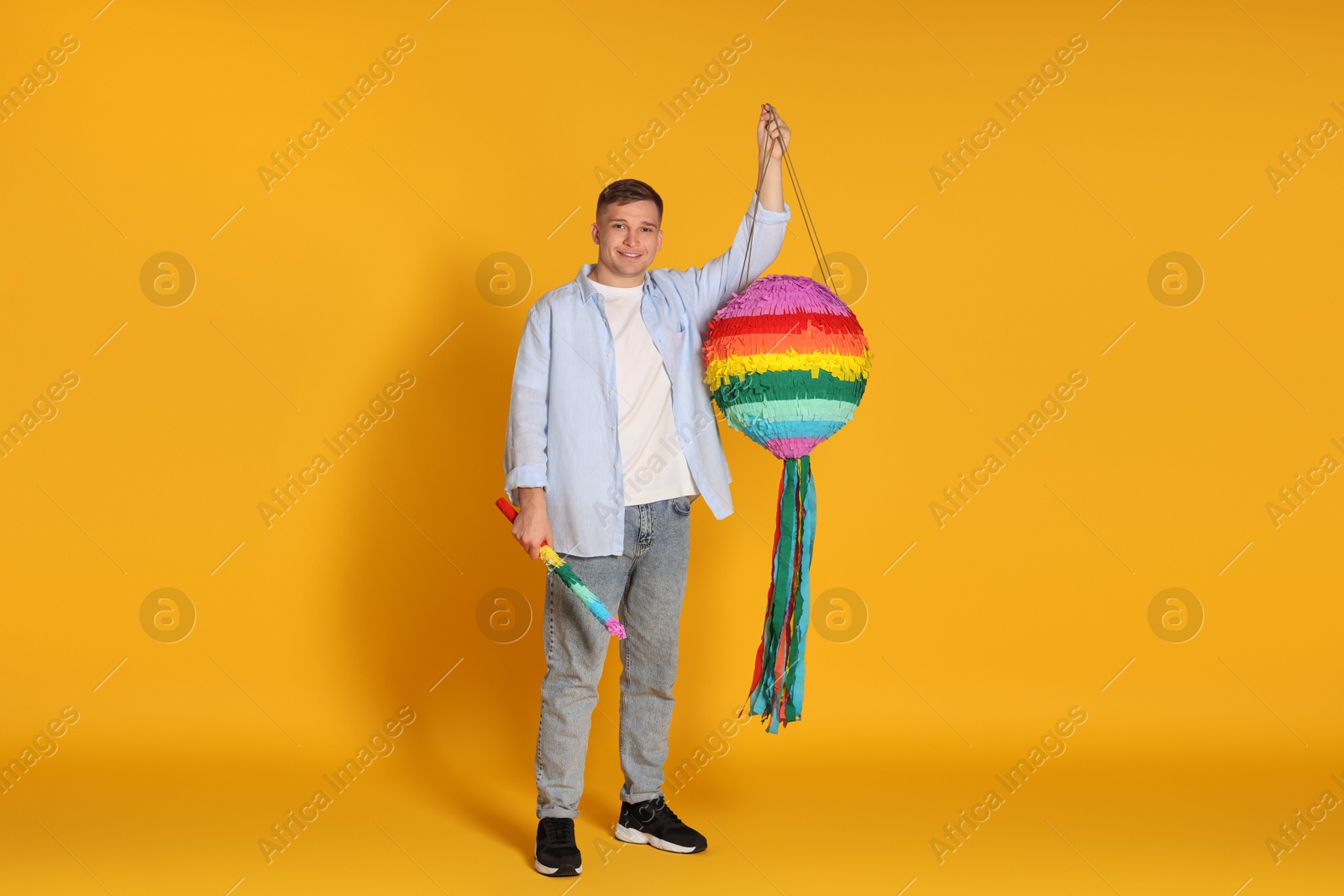 Photo of Happy man with colorful pinata and stick on yellow background