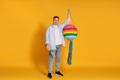 Photo of Happy man with colorful pinata and stick on yellow background