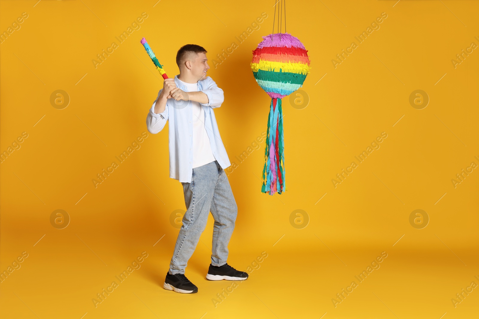 Photo of Happy man breaking pinata on yellow background