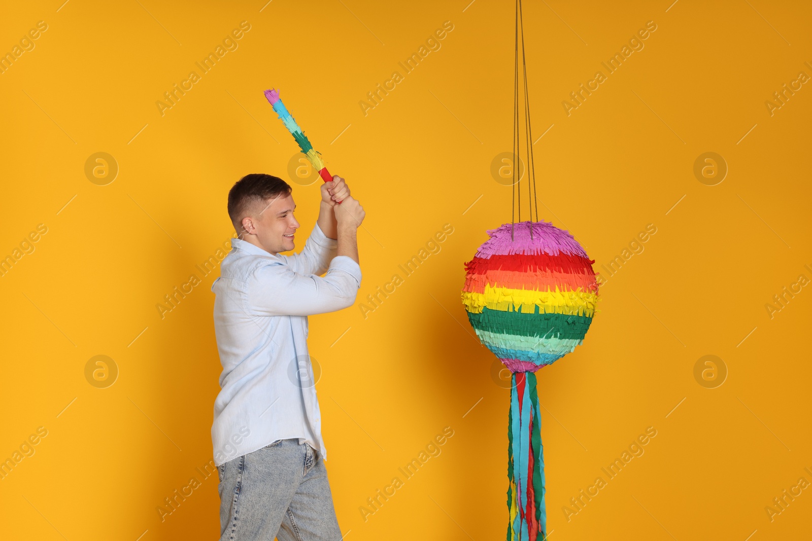 Photo of Happy man breaking pinata on yellow background