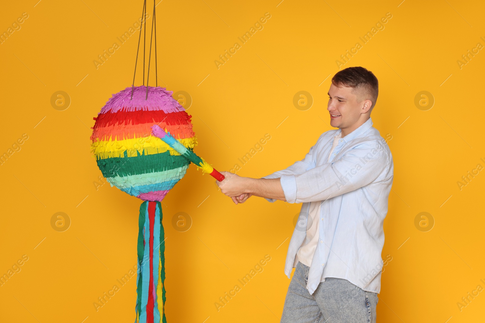 Photo of Happy man breaking pinata on yellow background