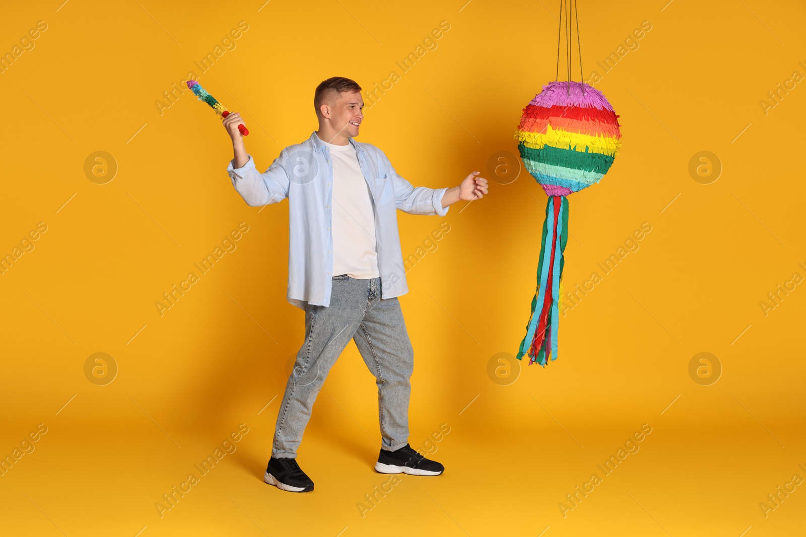 Photo of Happy man breaking pinata on yellow background