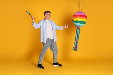 Photo of Happy man breaking pinata on yellow background