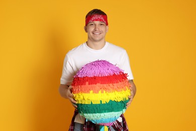 Happy man with colorful pinata on yellow background