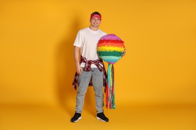 Photo of Happy man with colorful pinata on yellow background