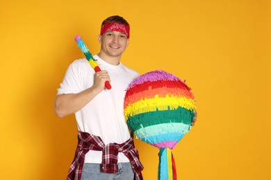 Photo of Happy man with colorful pinata and stick on yellow background