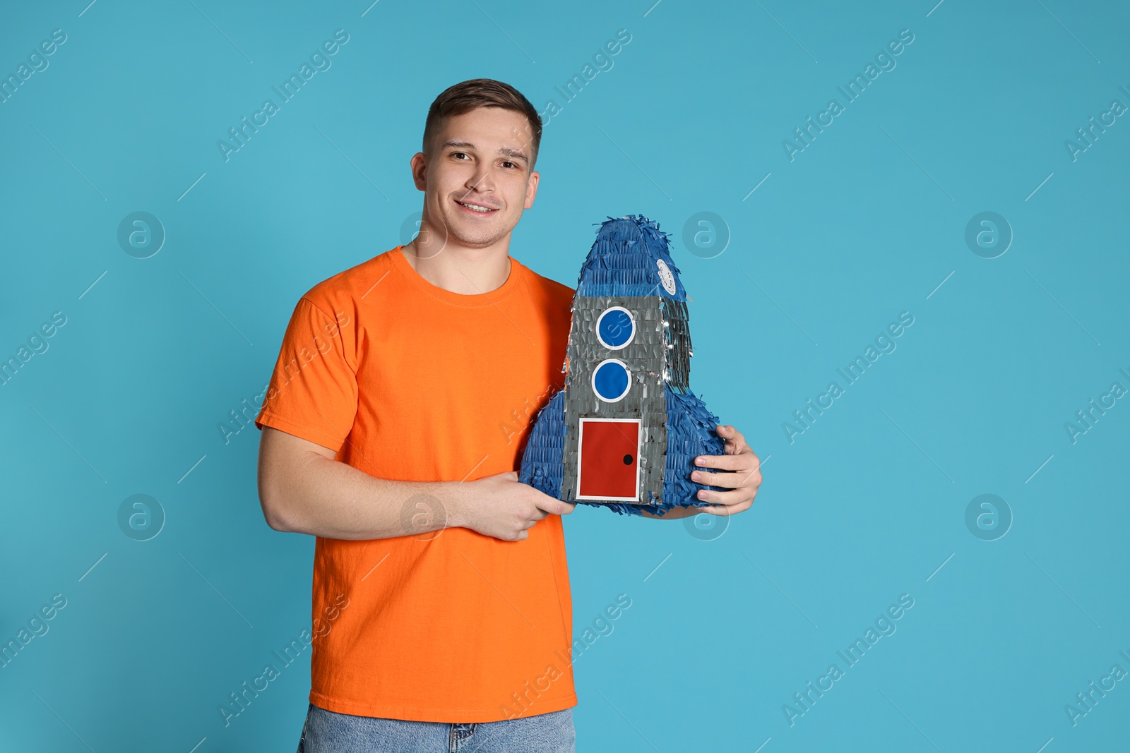 Photo of Happy man with pinata in shape of spaceship on light blue background. Space for text