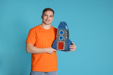 Photo of Happy man with pinata in shape of spaceship on light blue background. Space for text