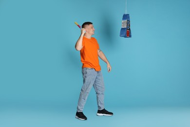 Happy man breaking pinata on light blue background