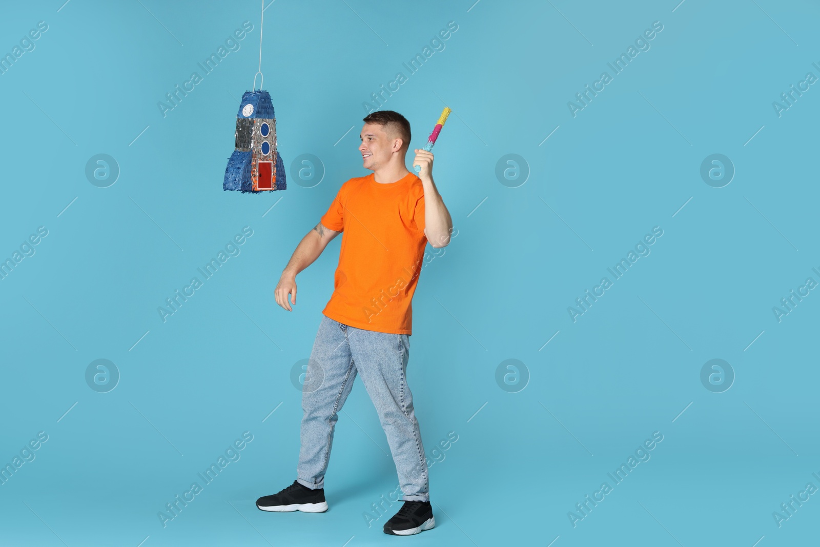 Photo of Happy man breaking pinata on light blue background