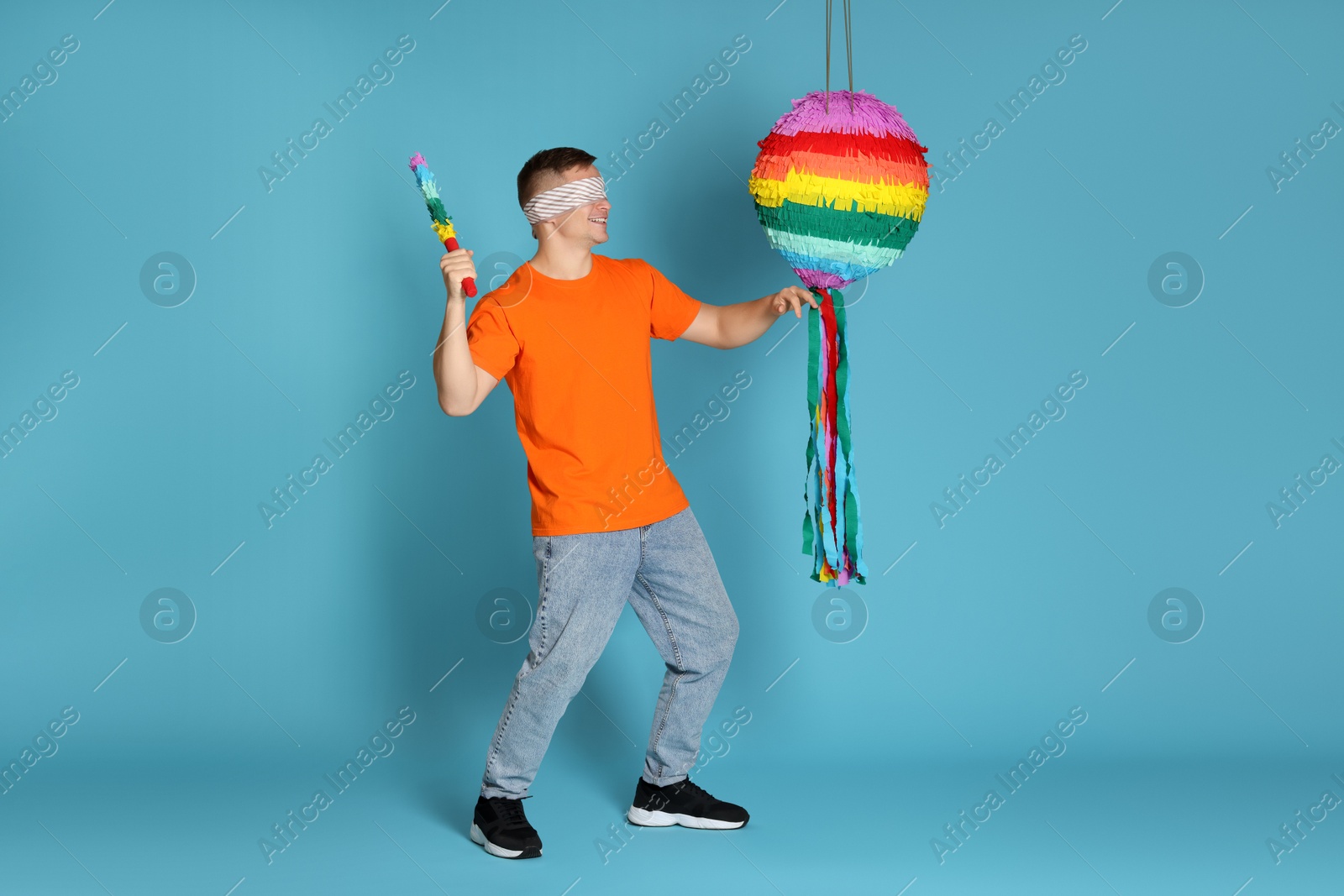 Photo of Man with tied eyes breaking pinata on light blue background