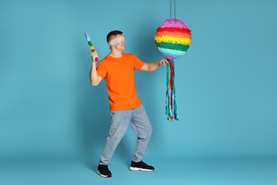 Photo of Man with tied eyes breaking pinata on light blue background