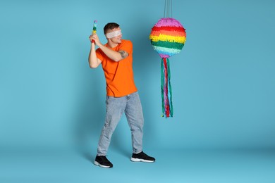 Photo of Man with tied eyes breaking pinata on light blue background