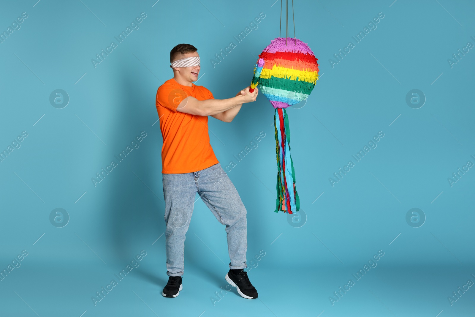 Photo of Man with tied eyes breaking pinata on light blue background