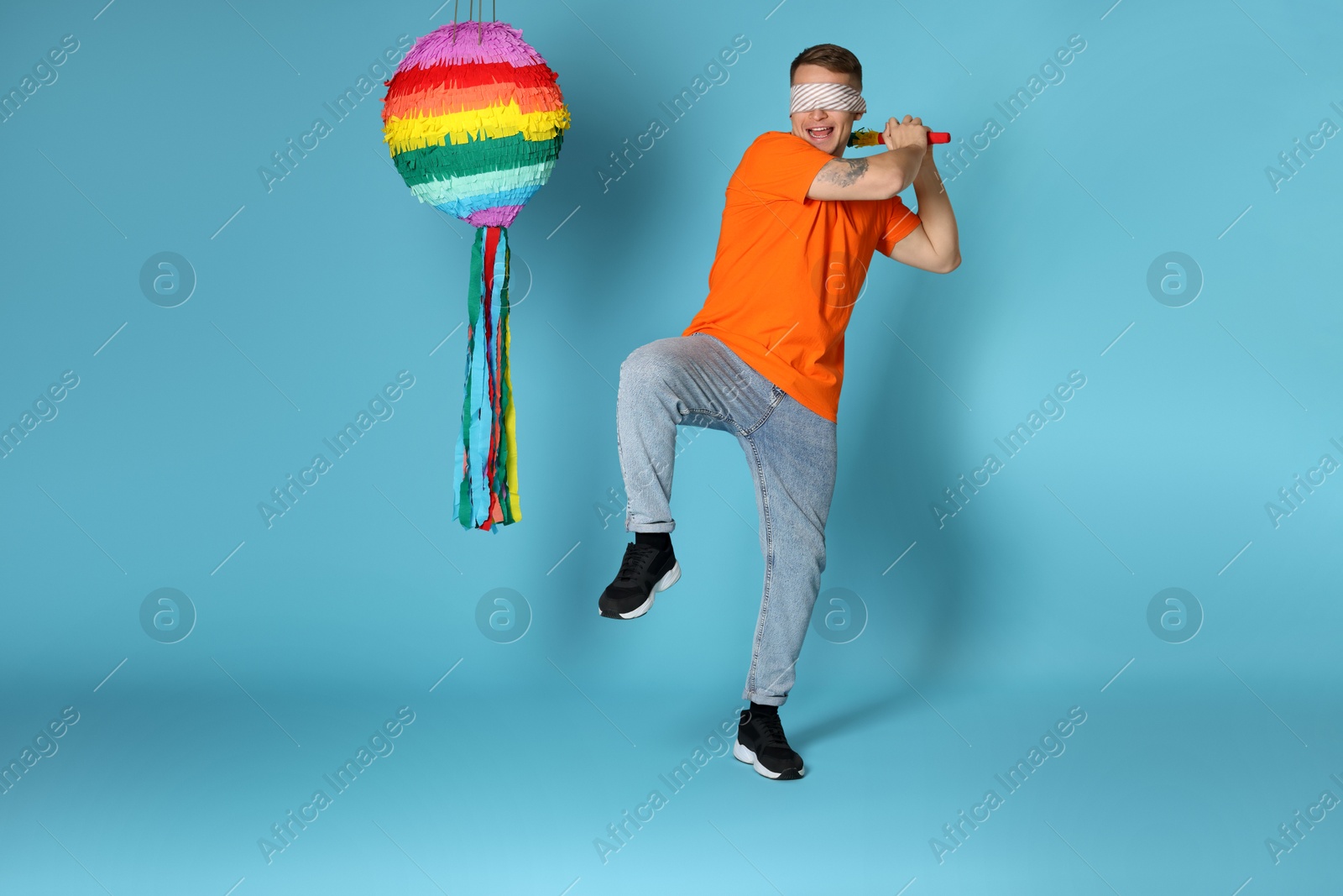 Photo of Man with tied eyes breaking pinata on light blue background