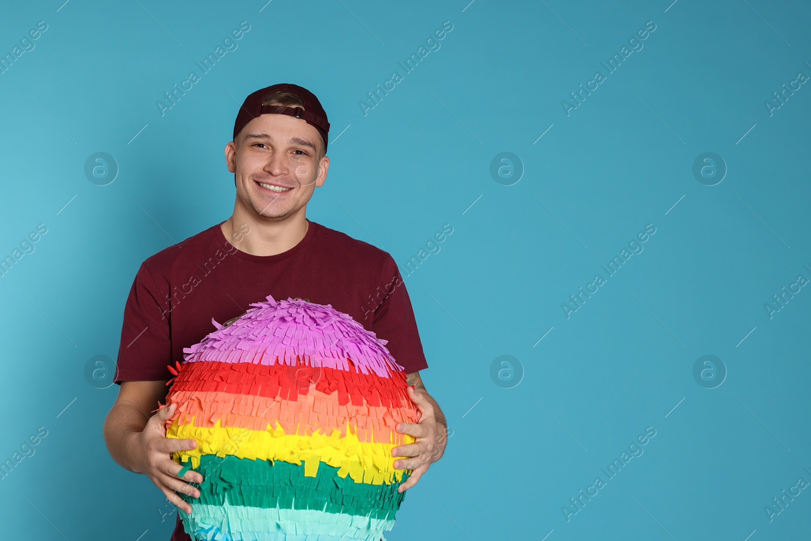 Photo of Happy man with colorful pinata on light blue background. Space for text