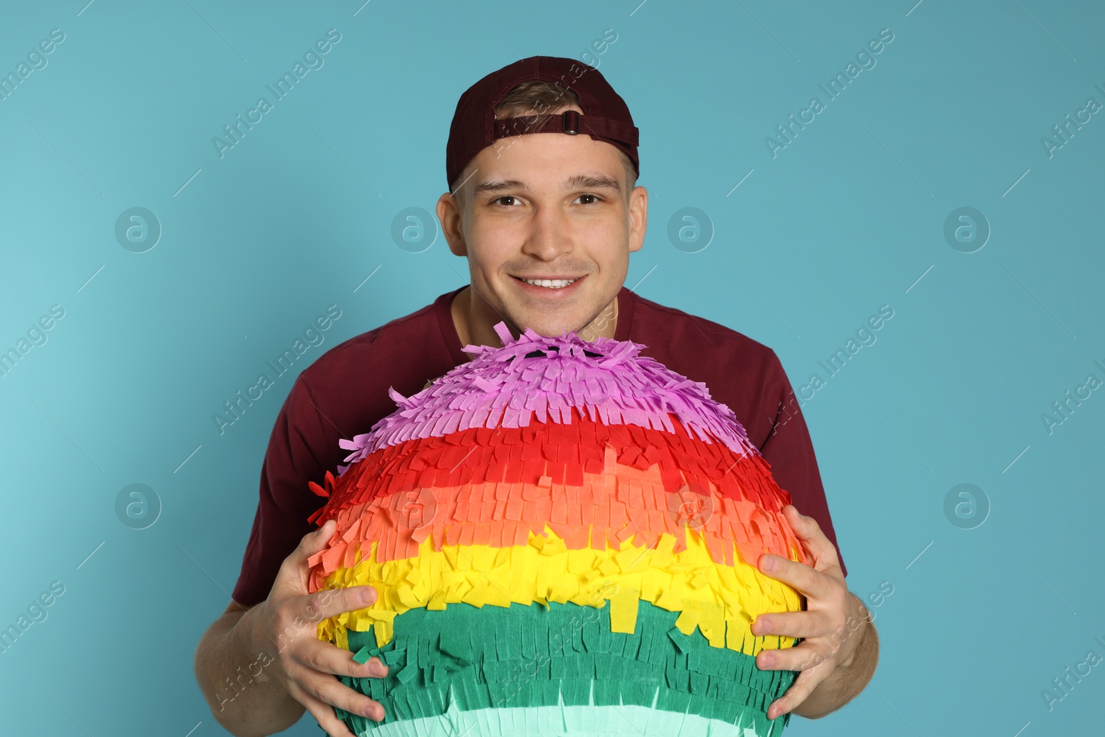 Photo of Happy man with colorful pinata on light blue background