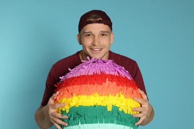 Happy man with colorful pinata on light blue background