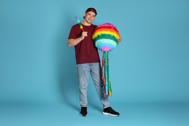 Photo of Happy man with colorful pinata and stick on light blue background. Space for text