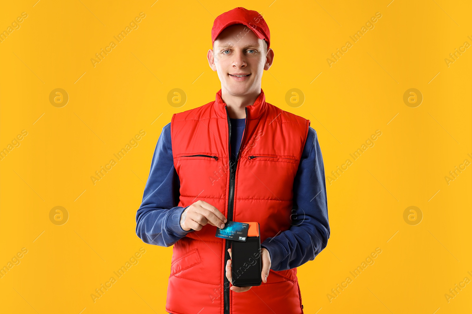 Photo of Happy courier with payment terminal and debit card on yellow background