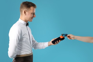 Photo of Waiter taking payment from client via terminal on light blue background