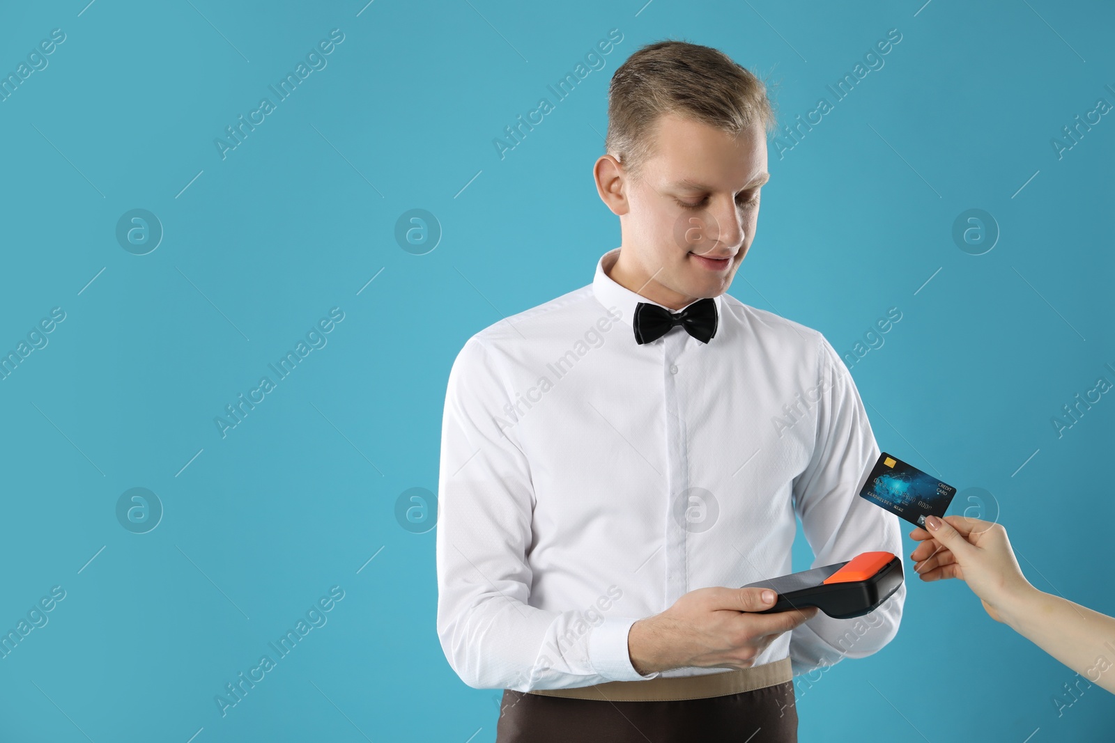 Photo of Waiter taking payment from client via terminal on light blue background, space for text