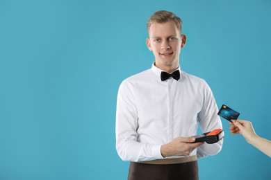 Waiter taking payment from client via terminal on light blue background, space for text