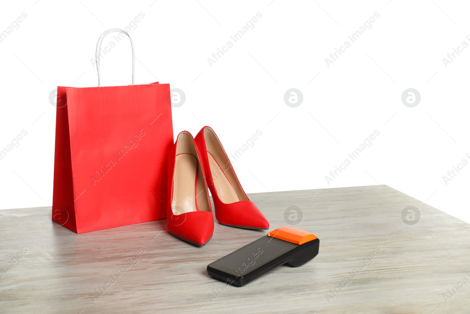 Photo of Payment terminal, shopping bag and high heeled shoes on wooden table against white background